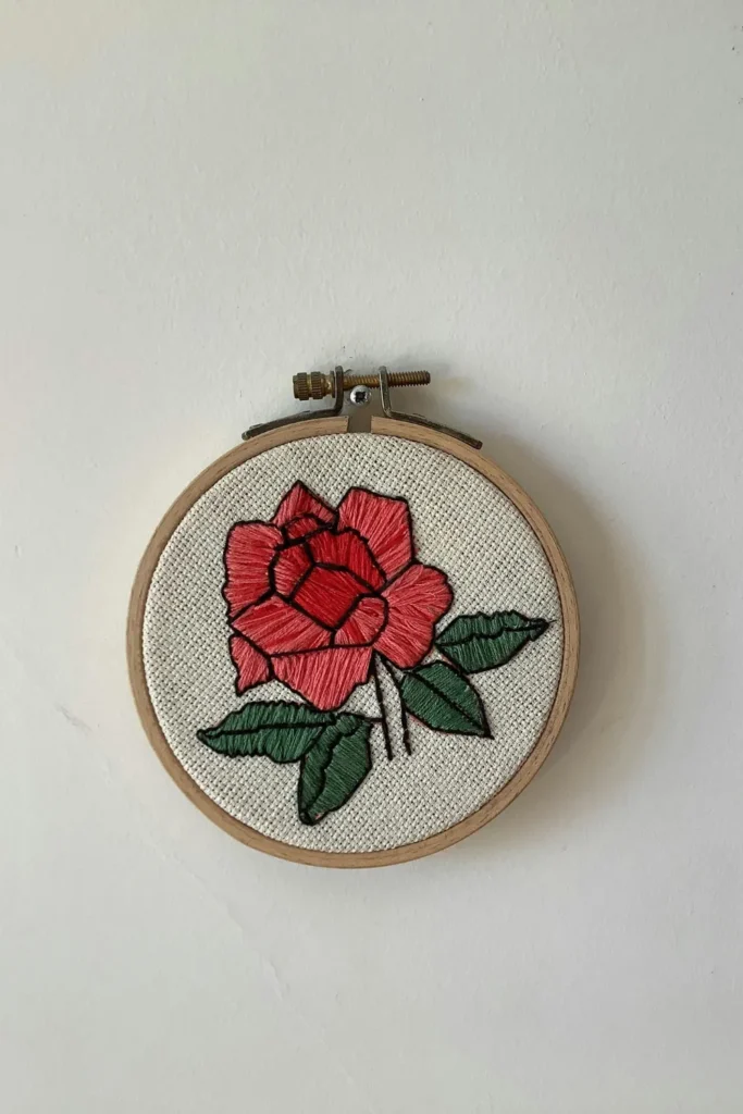 A beautifully embroidered rose flower displayed on a wooden-handled hoop, showcasing intricate stitching and vibrant colors wallpaper