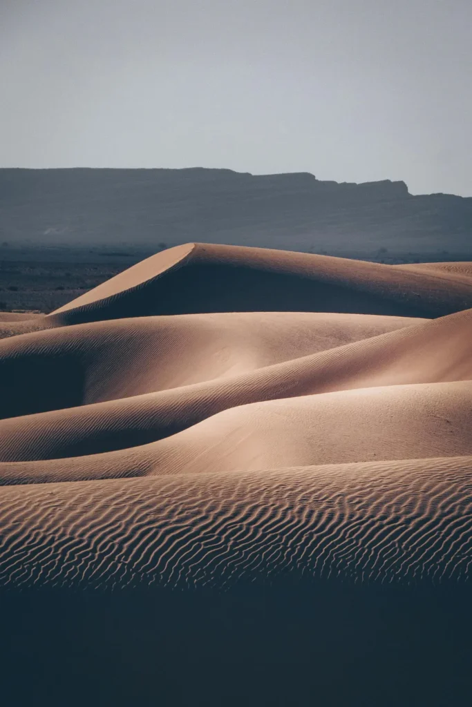  A vast desert landscape featuring rolling sand dunes with majestic mountains rising in the background wallpaper.